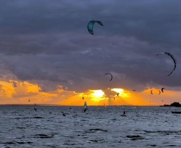Kitesurferzy na wodzie podczas zachodu słońca – dynamiczny kadr sportowy z bardzo efektownym niebem.