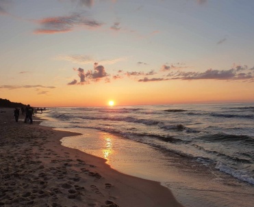 Zachód słońca nad plażą i morzem, z delikatnymi odbiciami światła na wodzie i spokojną kompozycją.