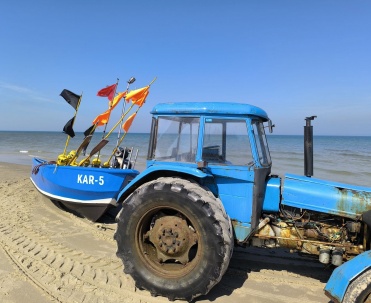 Niebieski traktor z łodzią na plaży w Karwi, charakterystyczny nadmorski widok i wakacje nad Bałtykiem.