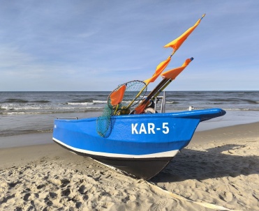 Niebieska łódź rybacka na plaży w Karwi, piasek, morze i charakterystyczny klimat nadmorskiej miejscowości.