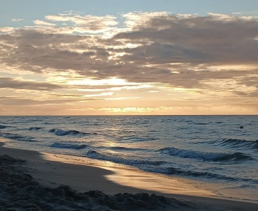 Fale Bałtyku o zachodzie słońca w Karwi, chmury, morze i spokojna plaża.
