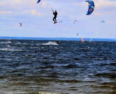 Kitesurferzy na wodzie podczas zachodu słońca – dynamiczny kadr sportowy z bardzo efektownym niebem.