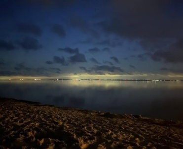 Ciemny, wieczorny kadr plaży z prześwitem światła nad horyzontem – bardziej nastrojowy niż pocztówkowy.