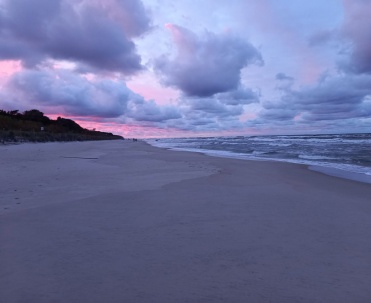 Plaża pod różowo-fioletowym niebem, z miękkim światłem i bardzo spokojną, pastelową atmosferą.