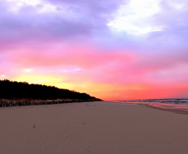 Plaża pod różowo-fioletowym niebem o zmierzchu, z pastelową kolorystyką i miękkim światłem.