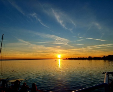 Spokojny zachód słońca nad wodą, z delikatnym zarysem łodzi i portowego klimatu po bokach kadru.