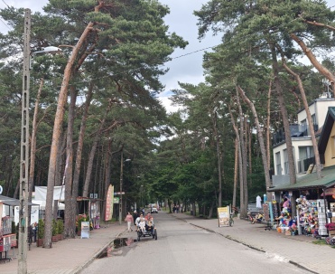 Ulica w centrum miasta Pobierowo z widocznymi sklepami i spacerującymi ludźmi.